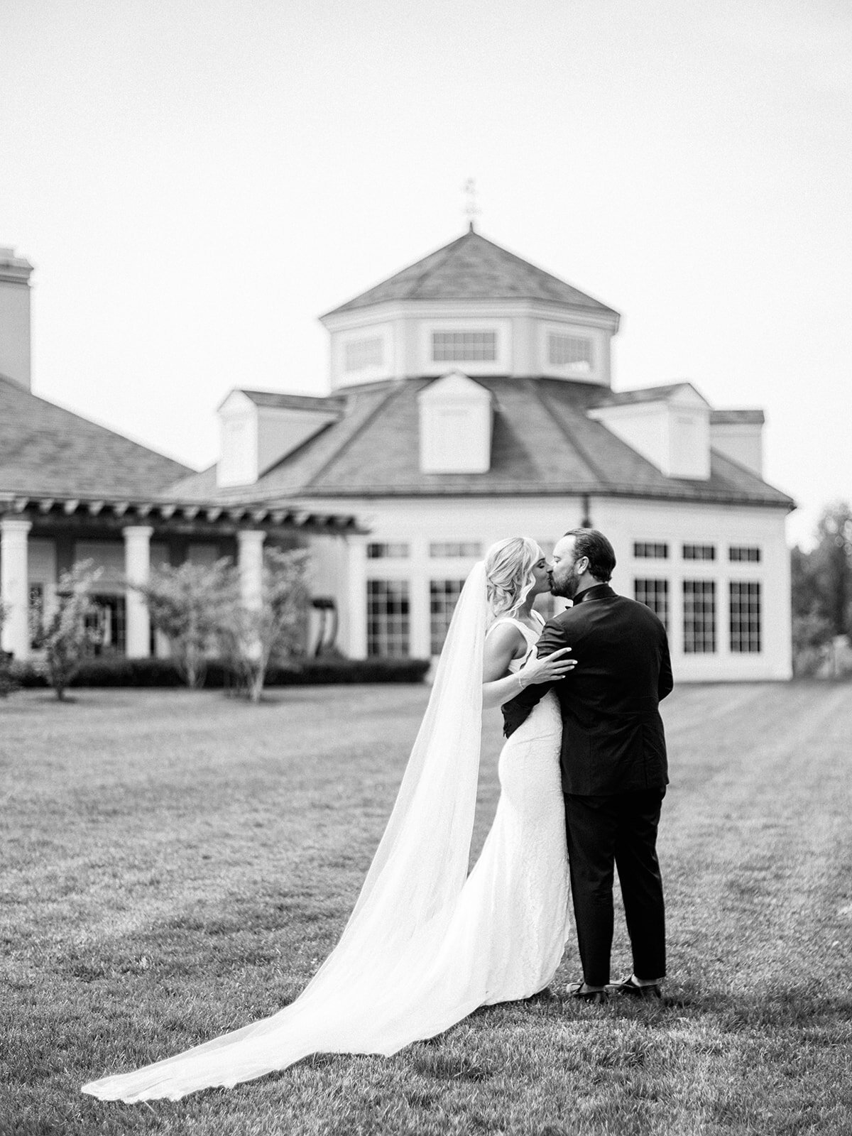bride and groom share a kiss in front of venue in this black and white image
