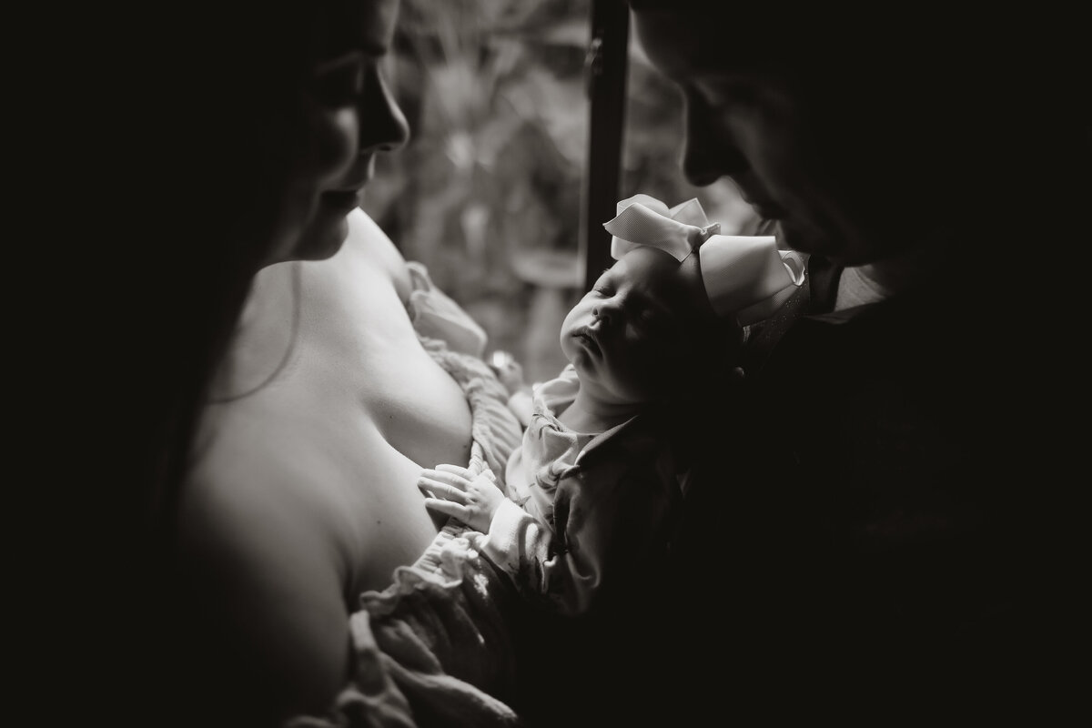 beautiful dark and moody lifestyle newborn portrait of a baby being held by her parents in her nursery