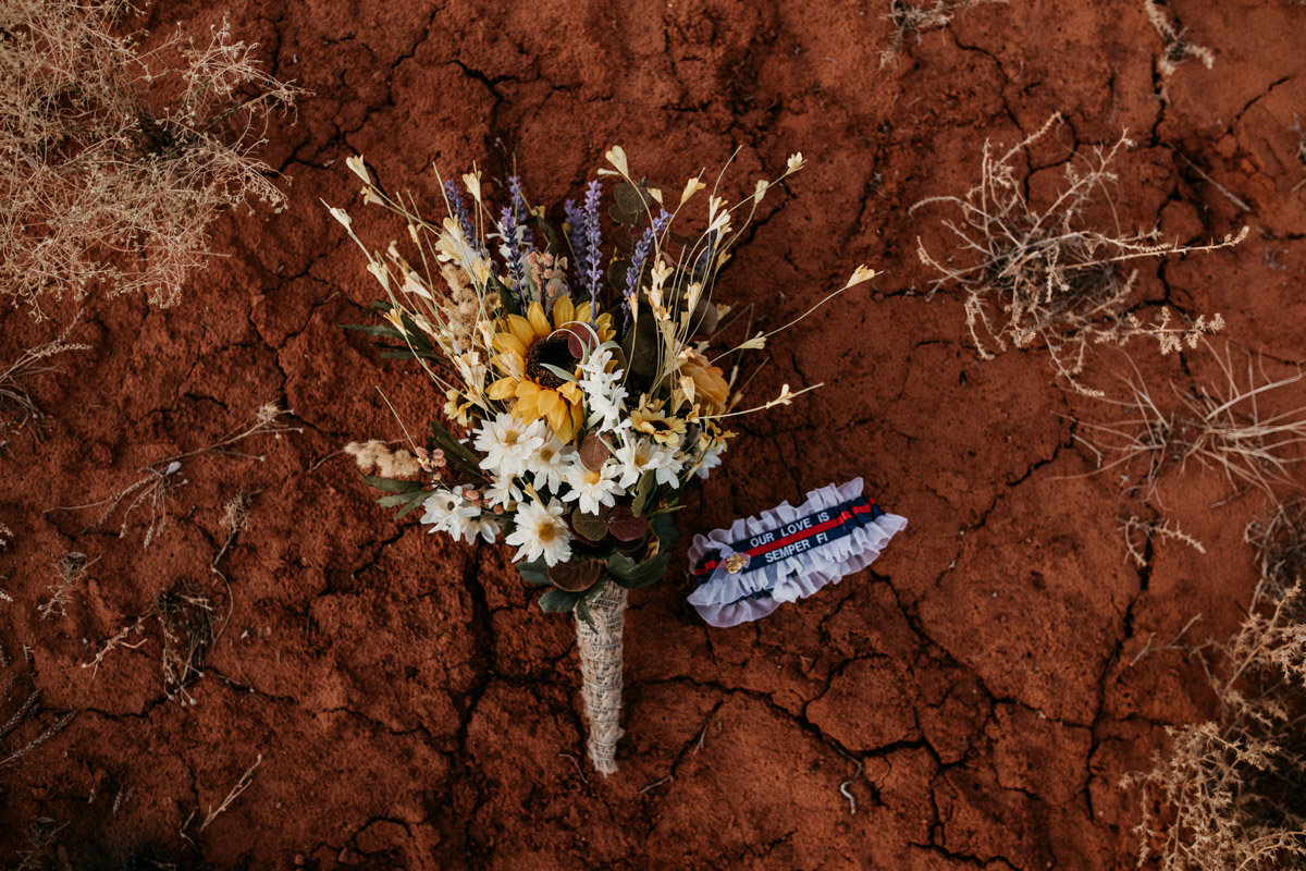 faux flower bouquet and garter laying on the red rock sand