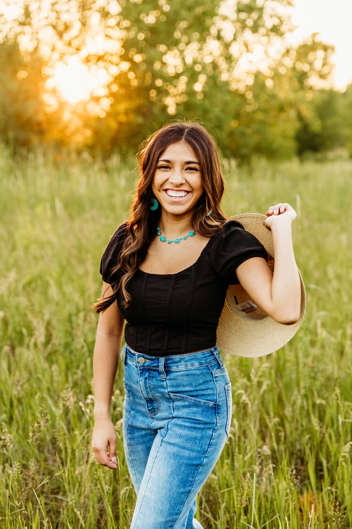 glowing portrait of a gorgeous high school girl laughing as she holds her sunhat in a beautiful meadow of grass near Appleton WI