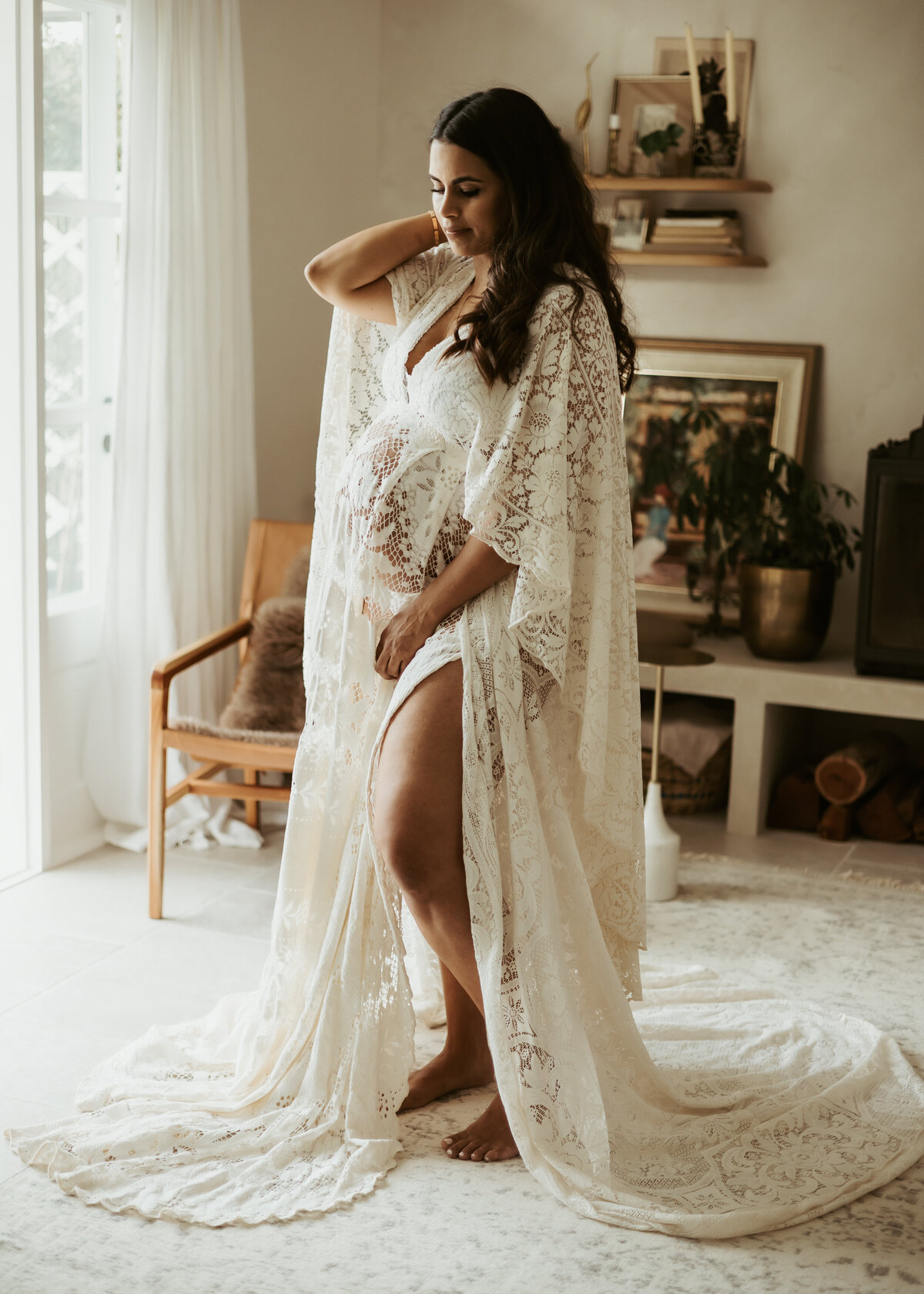 Mother to be in white long lace gown posing for in-home maternity photoshoot.