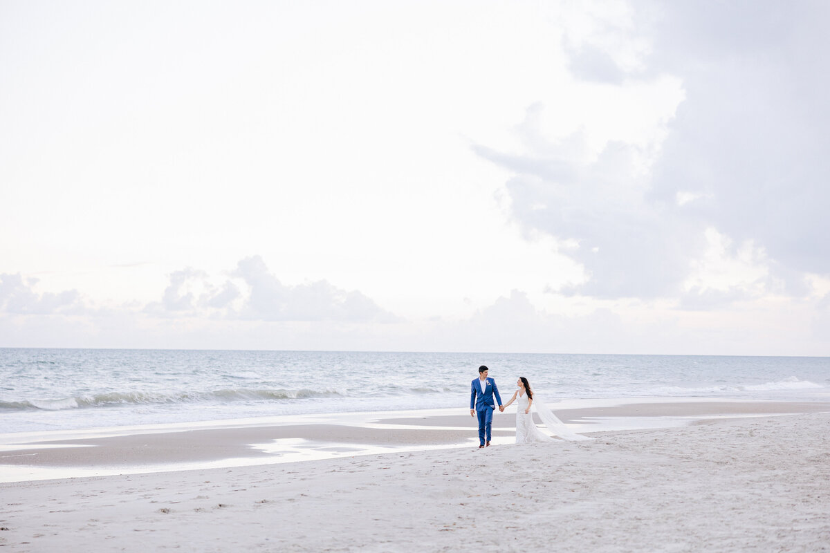 A couple in wedding attire, captured by a Destination Wedding Photographer, walking hand in hand along a serene beach.