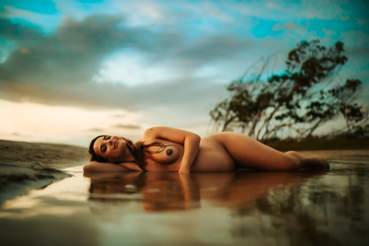 intimate fine art tasteful pregnancy portrait of a women laying nude in a inlet of water at the beach at sunset