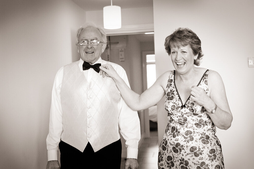 father of the bride in black tie and white waistcoat laughing with his wife