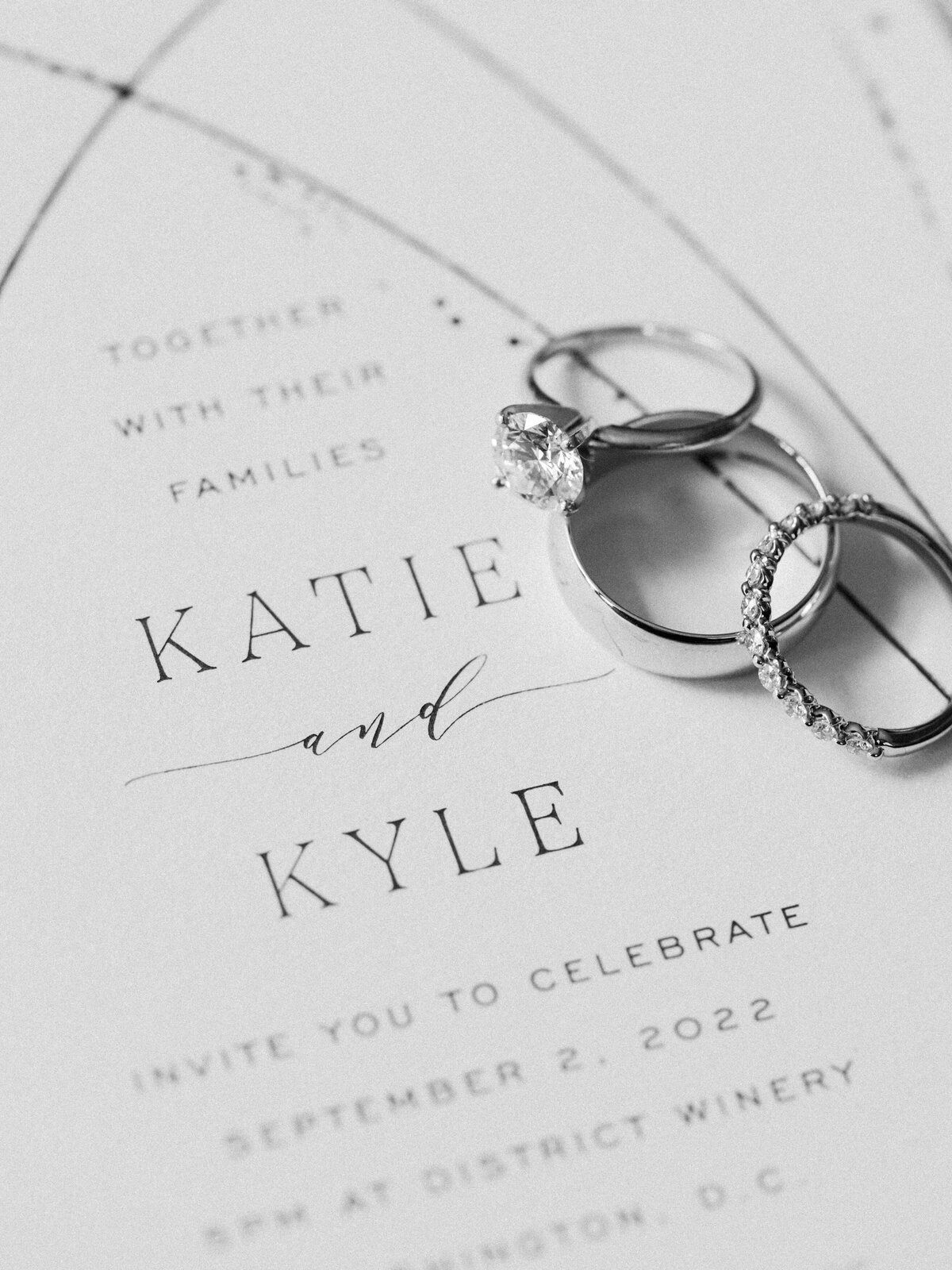 The wedding bands and engagement ring placed on top of a wedding invitation