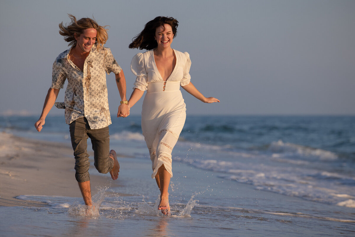 A couple holding hands and running along the beach