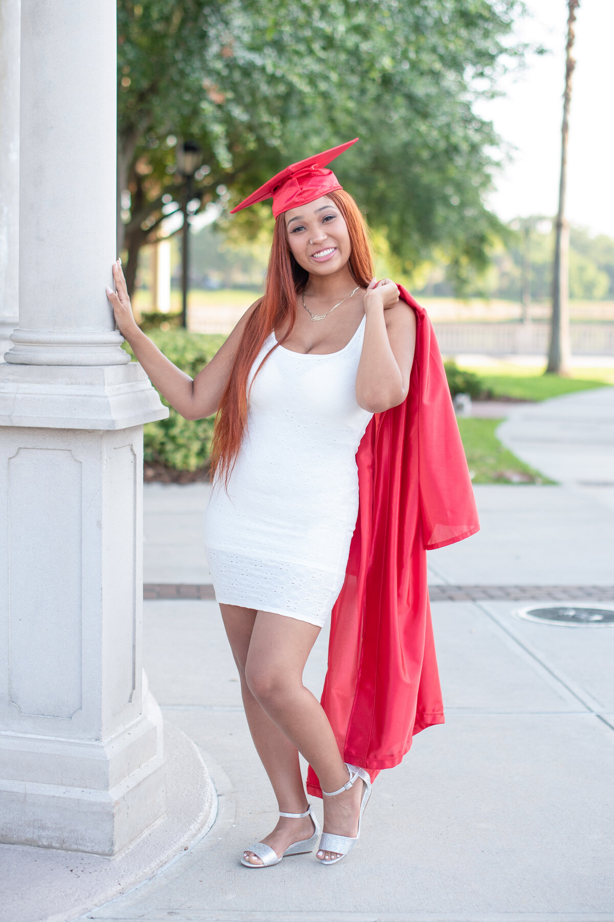 High school senior girl wearing cap holding gown over shoulder posing with pillar.