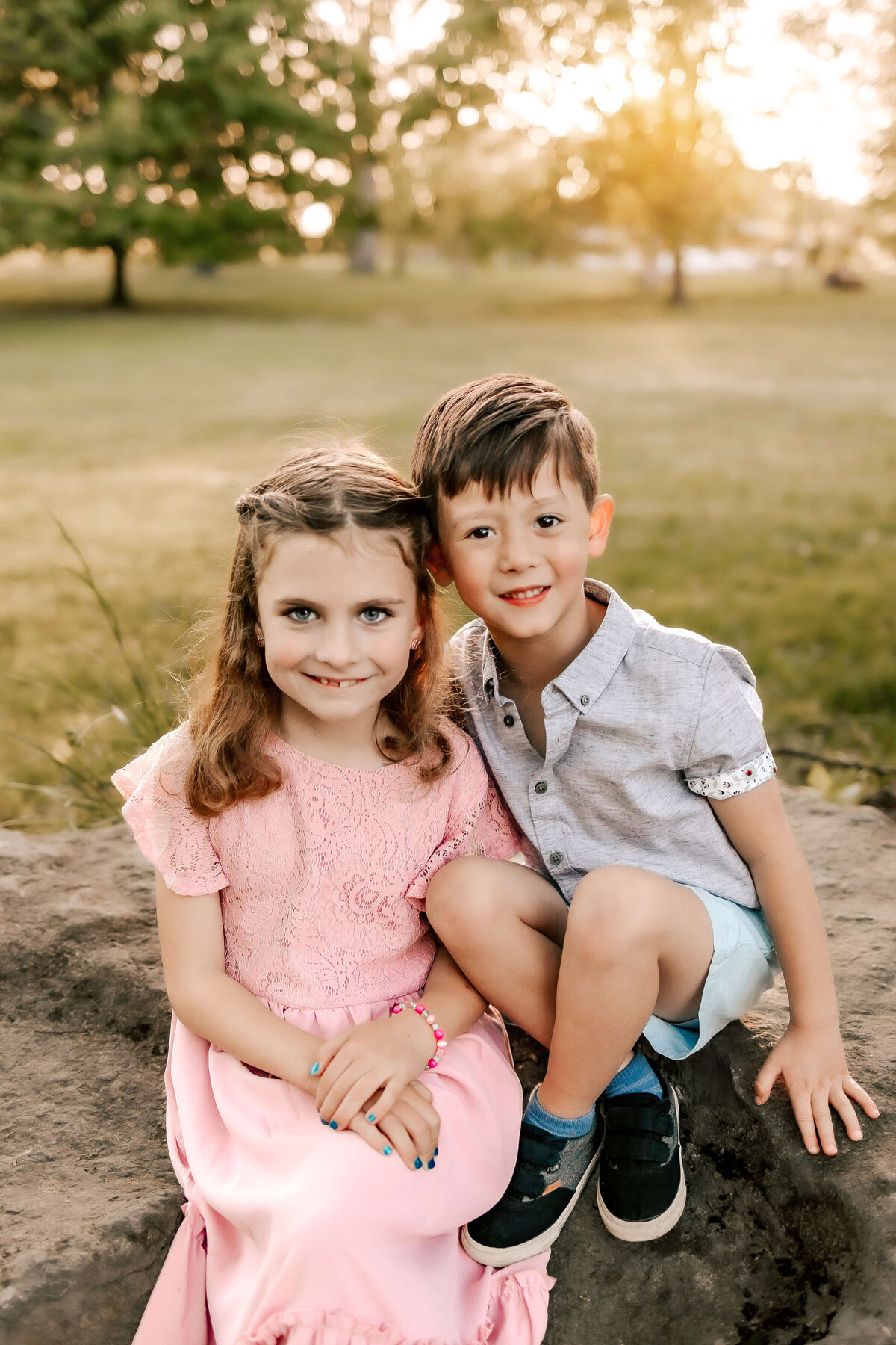 Siblings are sitting together on a big boulder  snuggled closely together as they smile for their family photos.