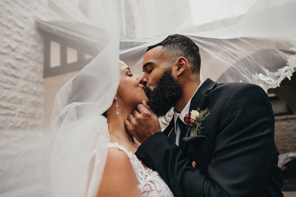 close up of a bride and groom kissing with veil draped over them