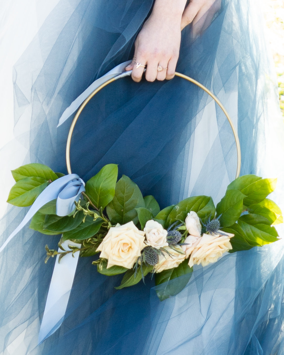 Detail shot of loop bouquet with roses in front of a white dress with blue tulle