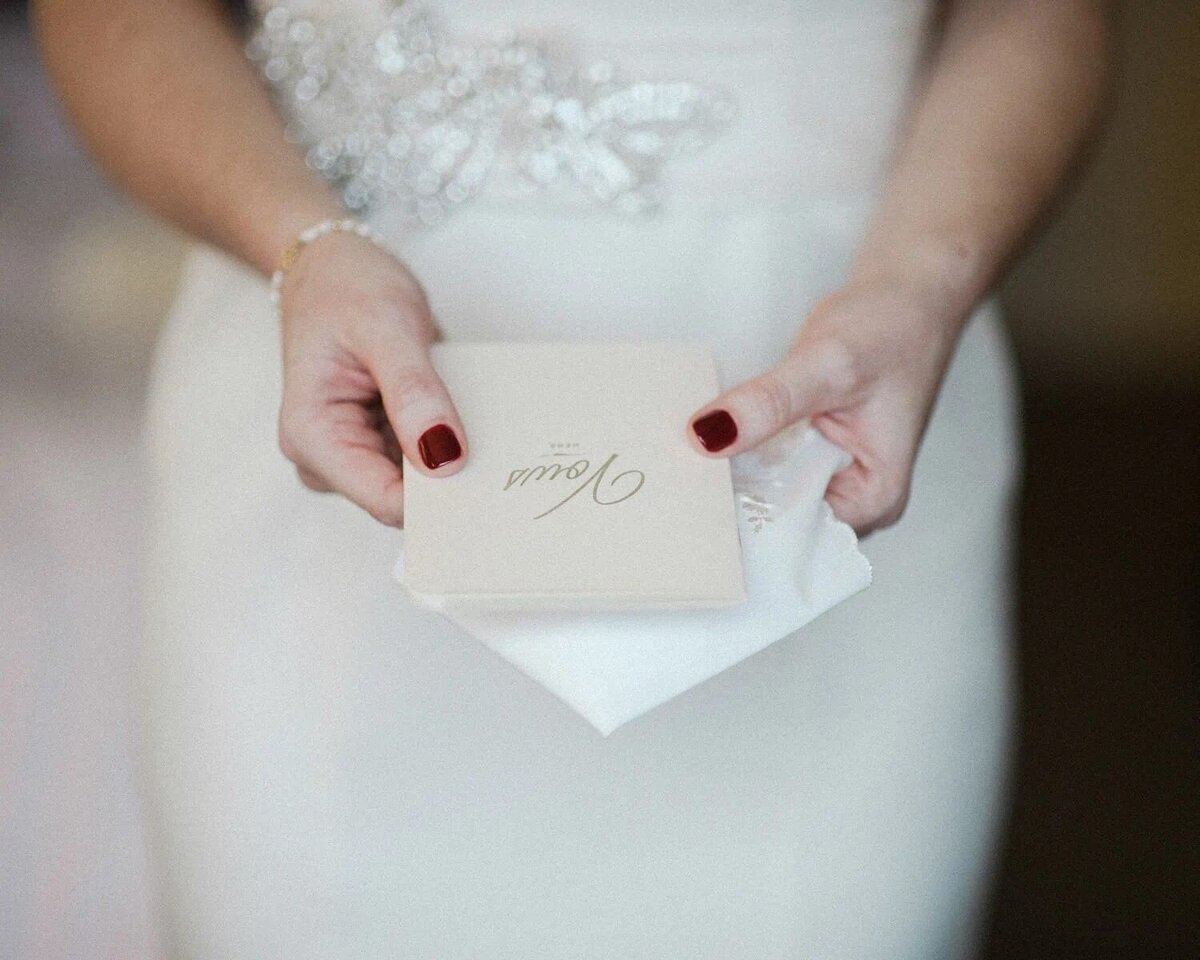 A close-up of a bride's hands holding a folded wedding invitation