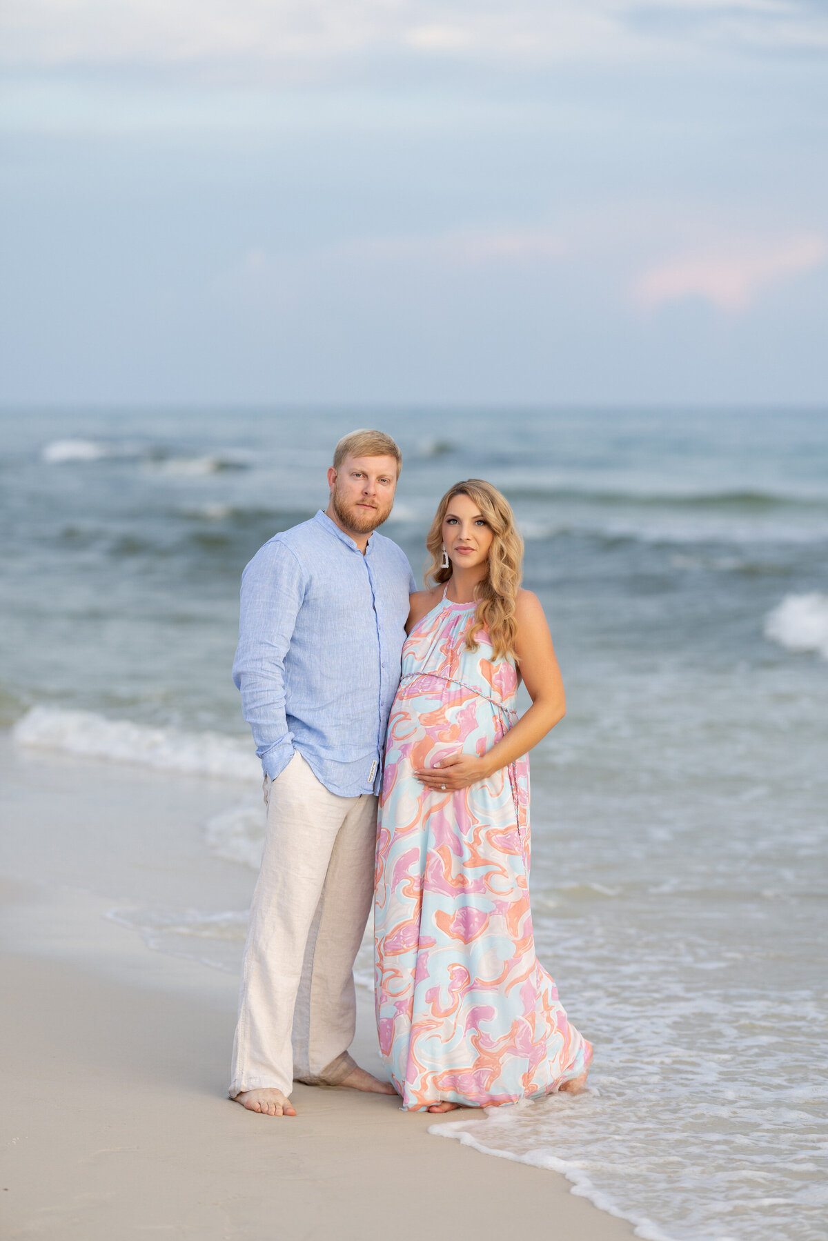 A pregnant couple standing along the water's edge