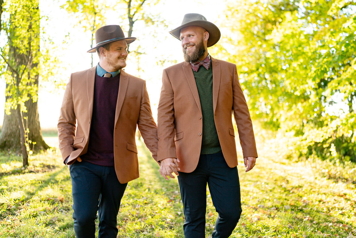 Men in cowboy hats hold hands and walk in the sunset.