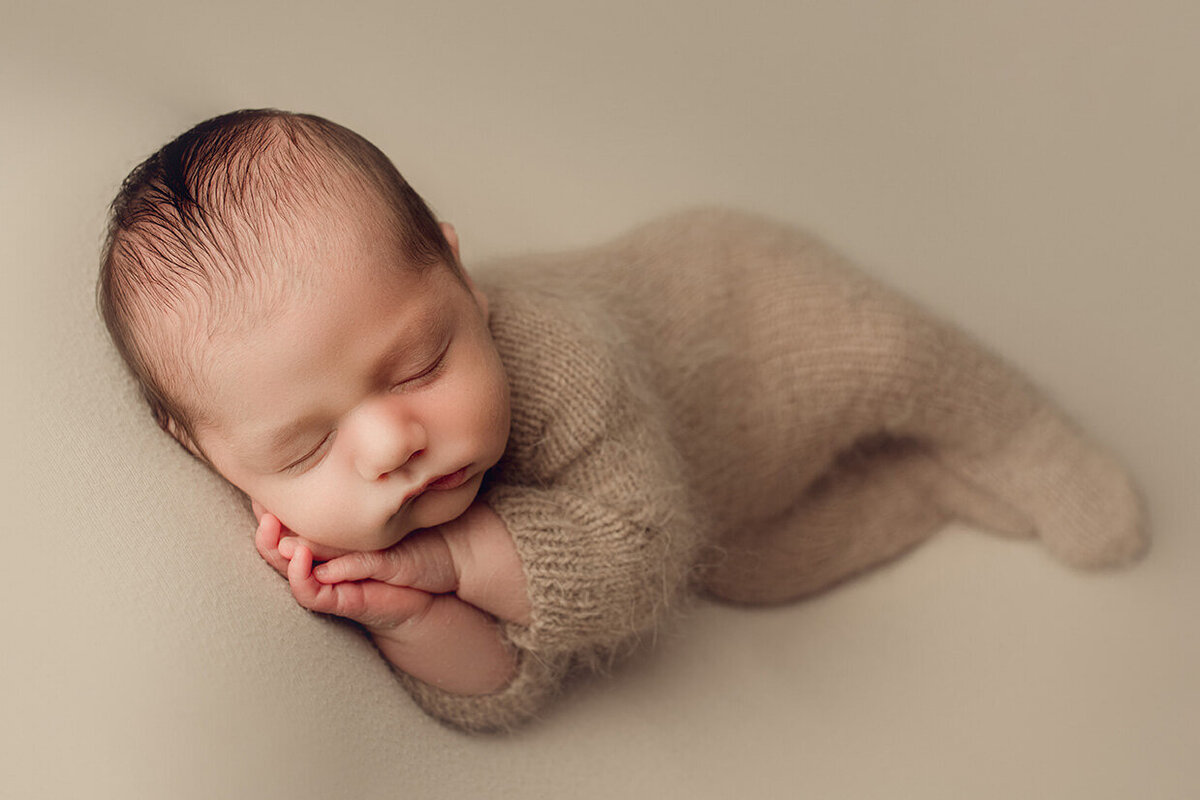 baby boy sleeping in a brown knitted romper with both hands under chin