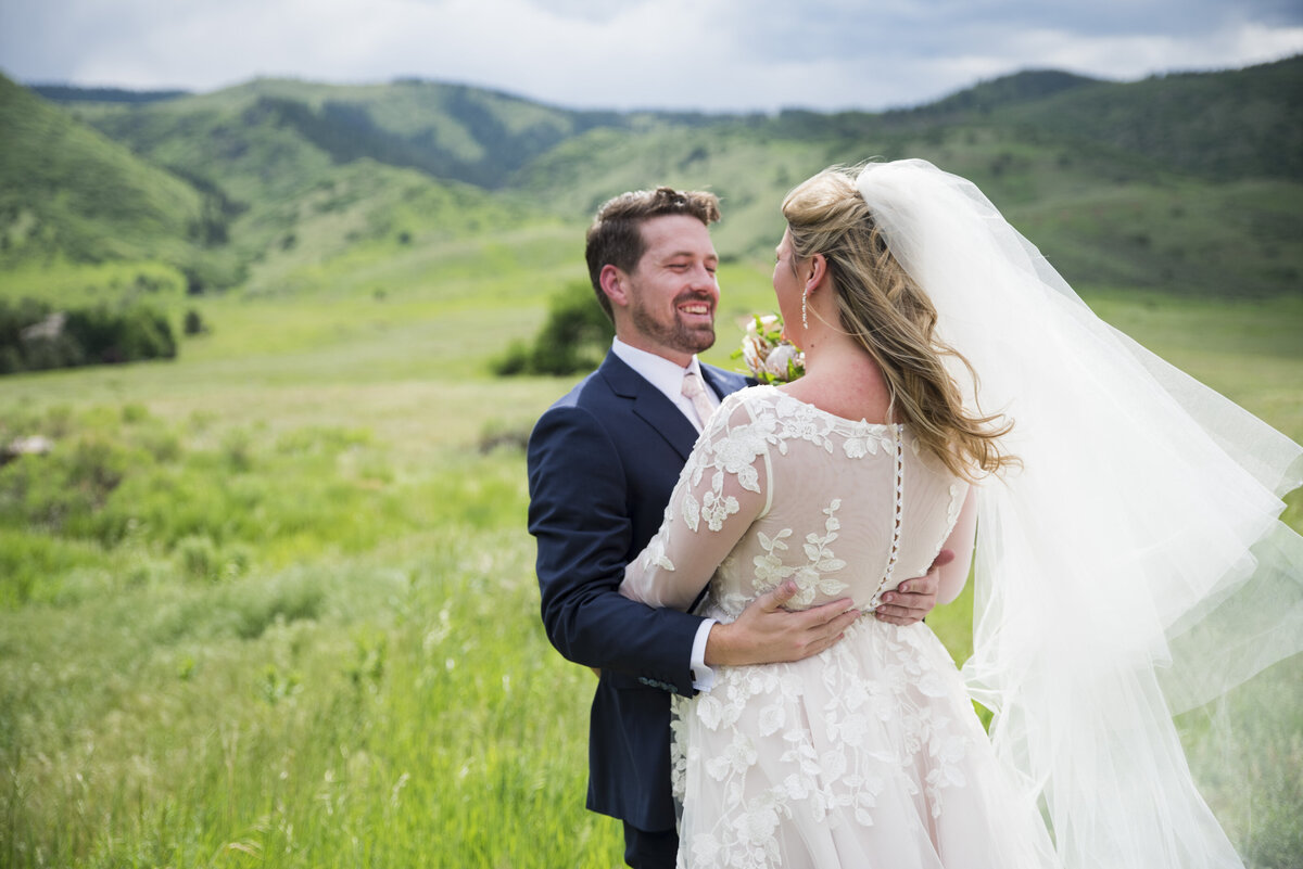 A groom embraces his bride and smiles during their first look at The Manor House with the rolling Colorado hills in the background.