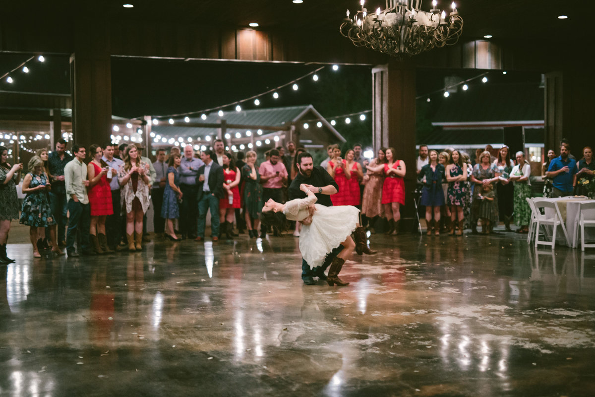 Groom dips bride during first dance at reception while guests cheer on at The Grande Hall at Hoffman Ranch wedding venue