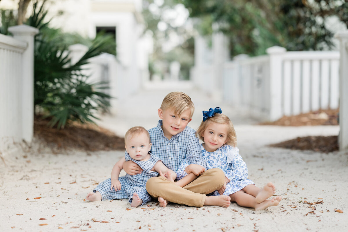 Three small kids sitting on a sandy path together