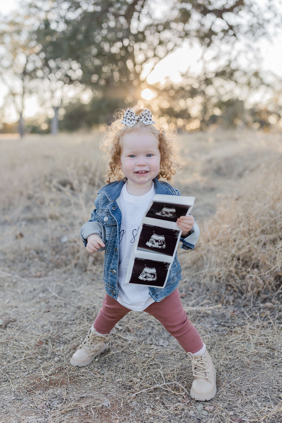 beautiful red head little girl holding up sonogram during pregnancy announcement photoshoot