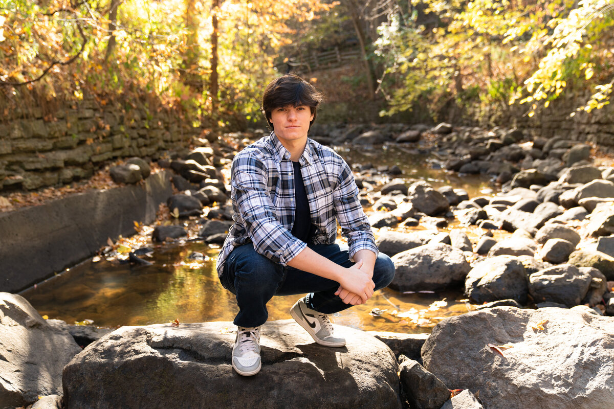 High school senior guy crouches on a rock for his senior picture