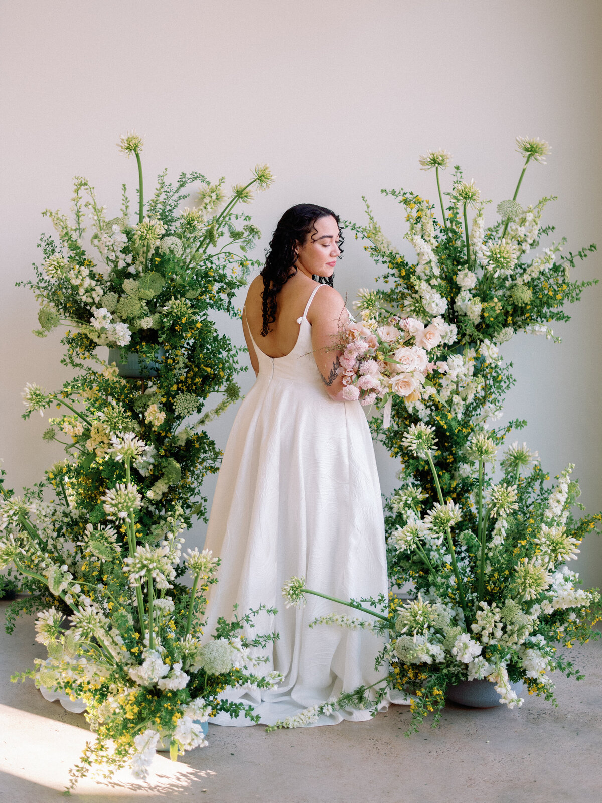 A bride stands in the middle of a large floral installation cascading around her.