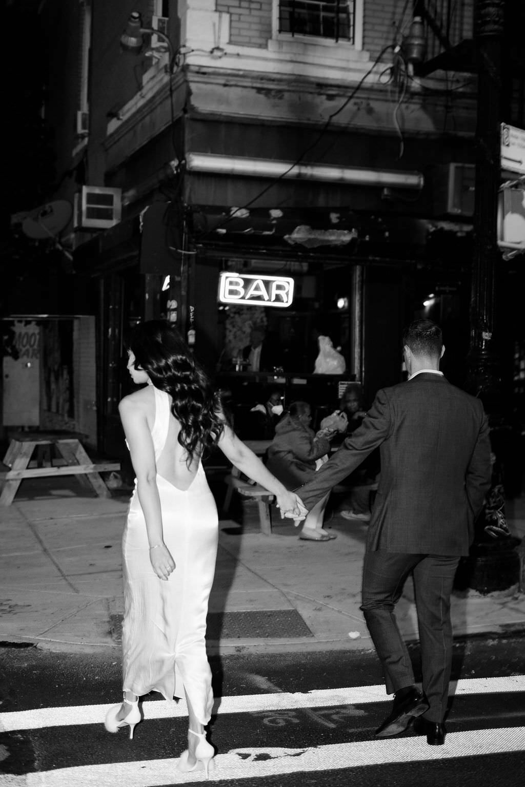 black and white photo of couple holding hands and walking across a city street
