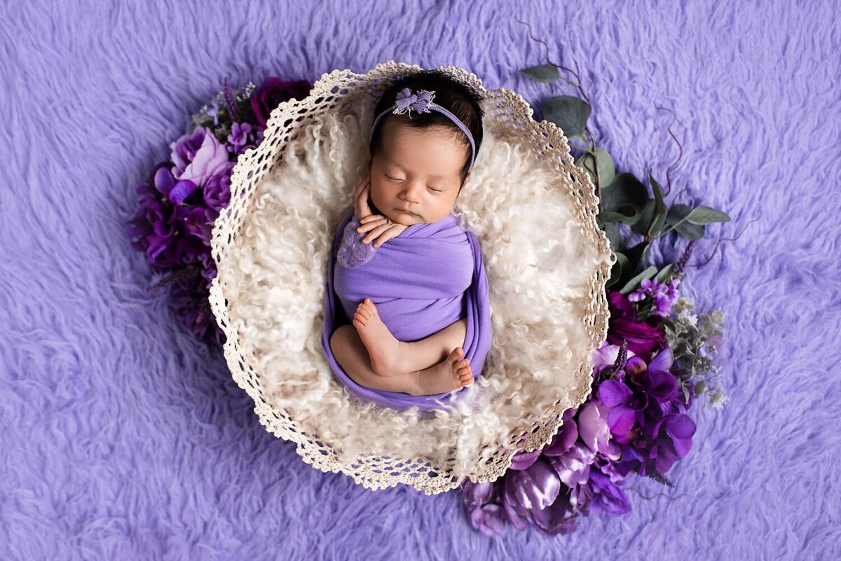 Newborn girl in lace basket with lavender flowers