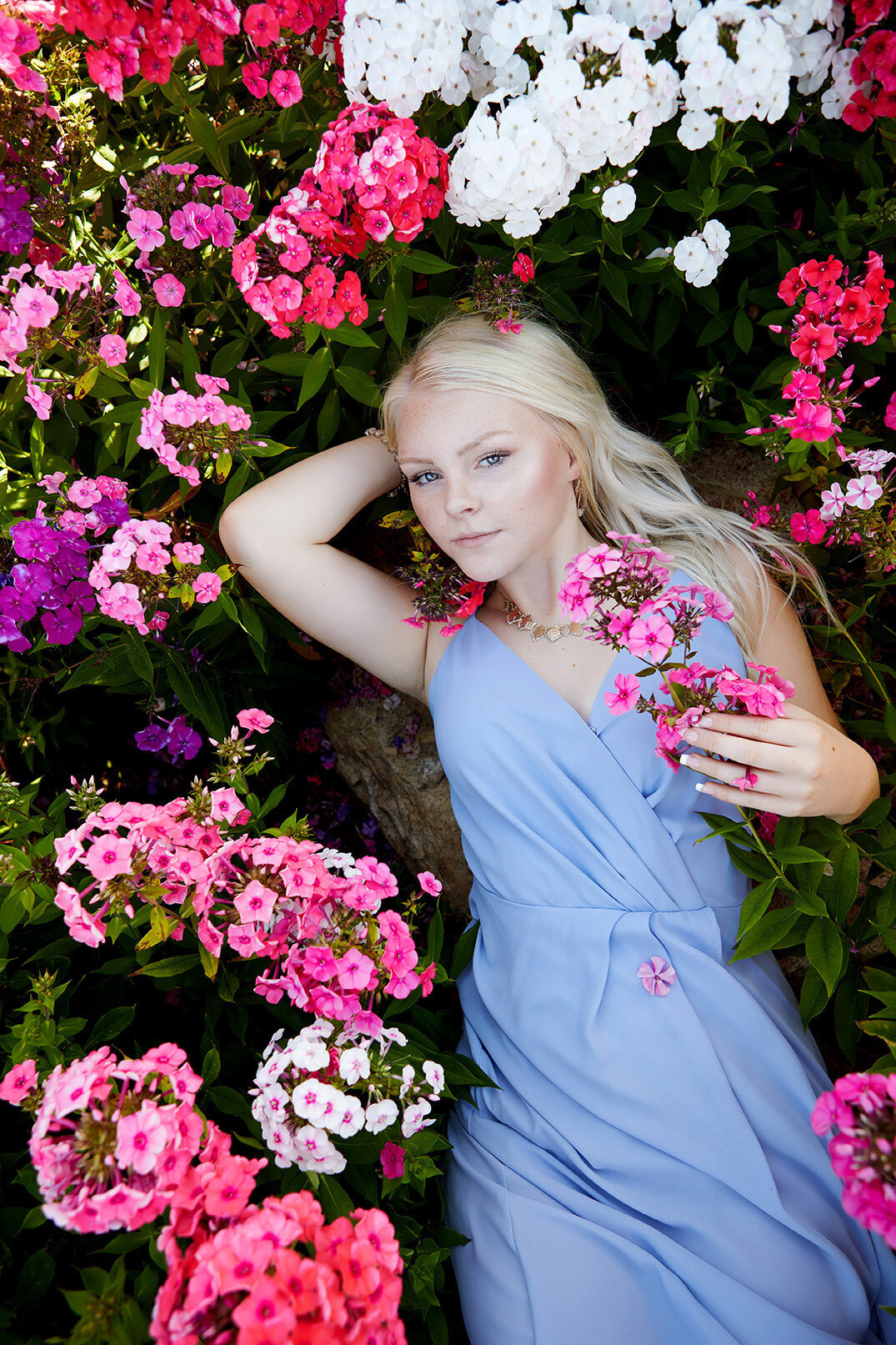 Blonde young woman laying on her back surrounded by phlox flowers looking up captured by Studio 64 Photography.