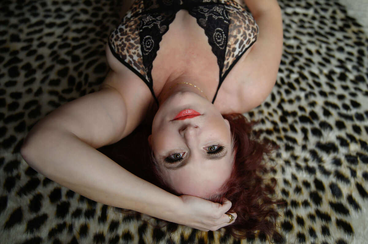 Red haired woman laying on a leopard rug with her hand in her hair