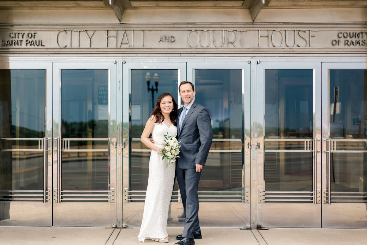 bride and groom stand in front of doors of city hall st paul minnesota