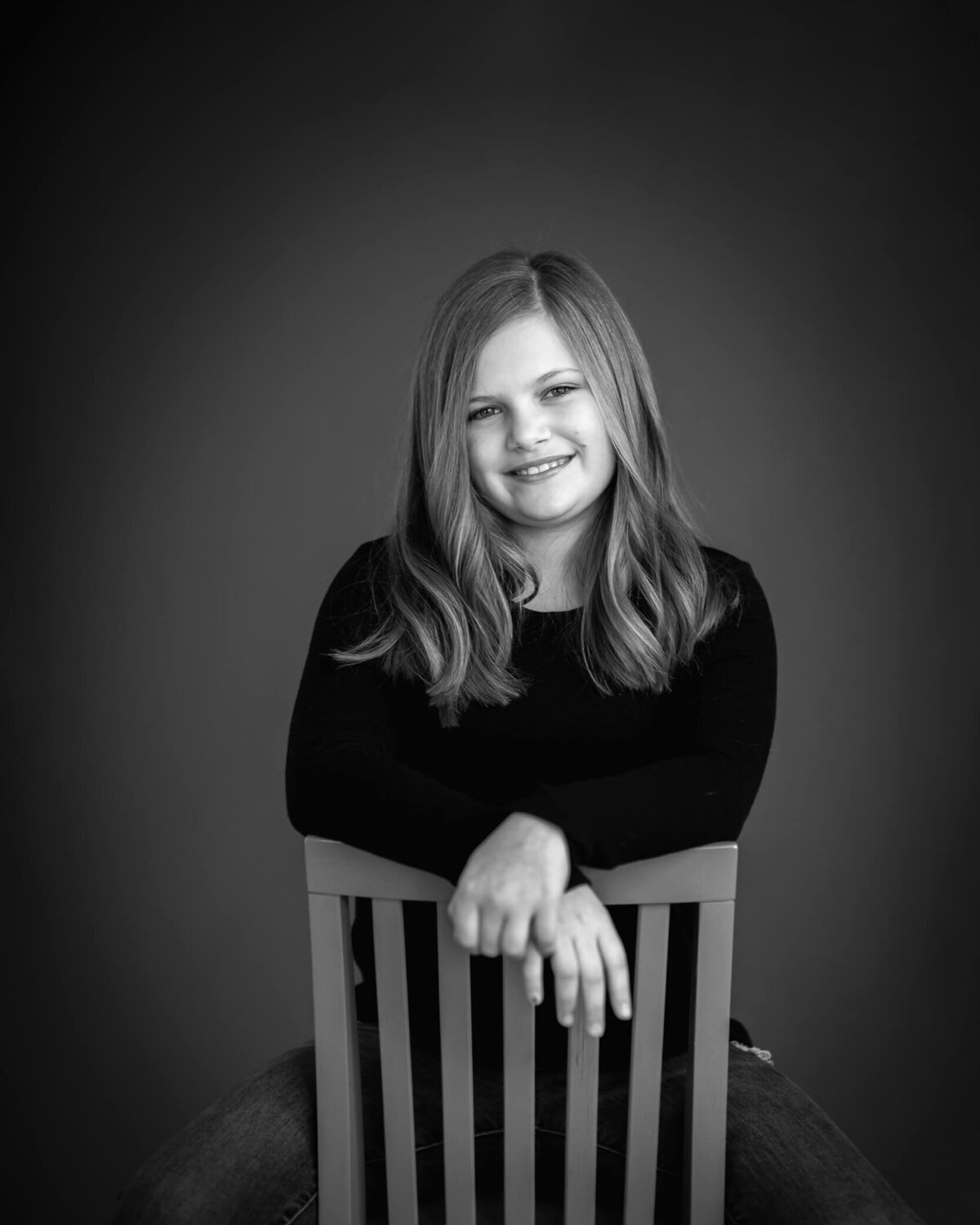 10 the birthday studio portrait of a girl in black and white with a dark background sitting backwards on a chair