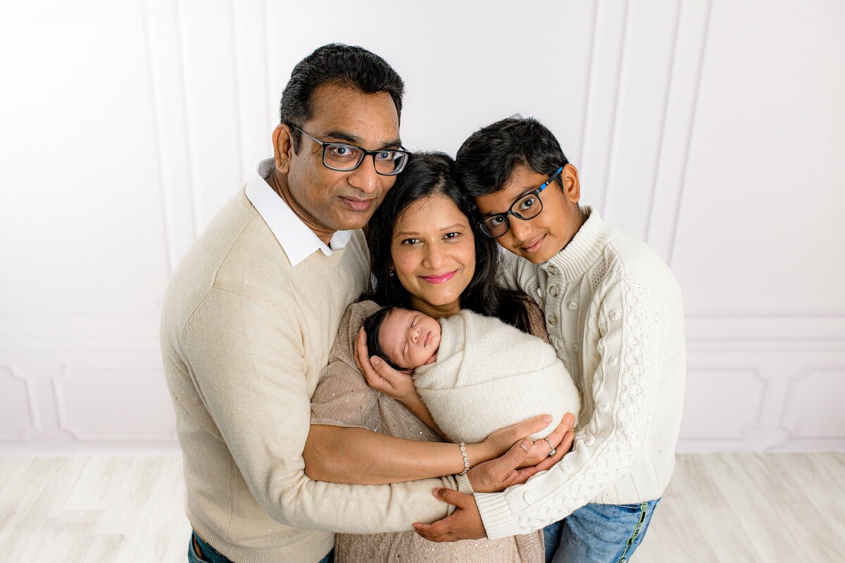 family f three snuggled in for a studio newborn portrait with their new son wrapped in cream between them