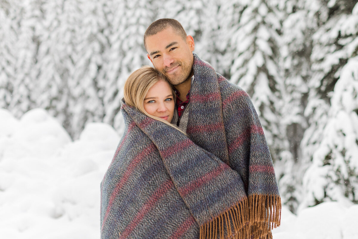 Beautiful couple cuddling under blanket at snow engagement session at Snoqualmie Pass near Seattle WA photo by Joanna Monger Photography