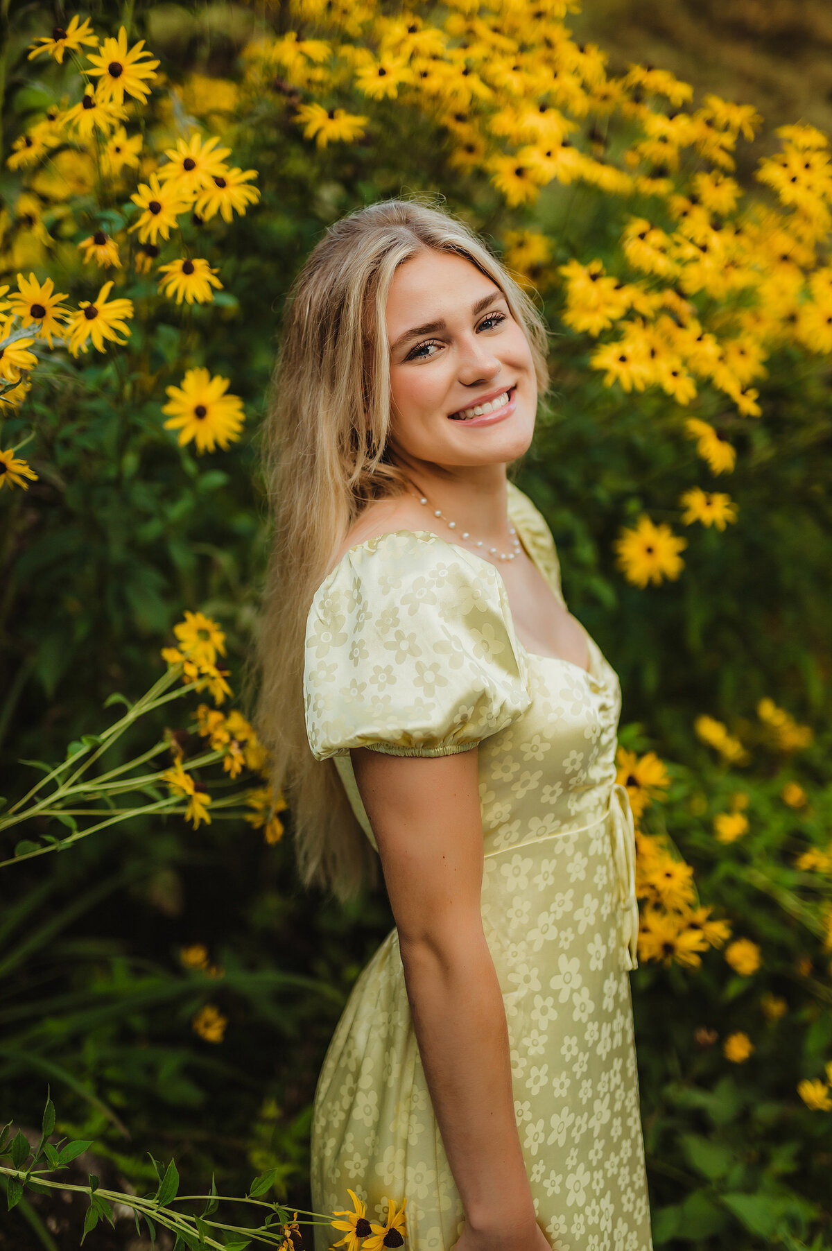 A student from Brookfield Central High School stands in a field of black-eyed susan flowers in Delafield, WI wearing a floral sundress for her senior pictures.