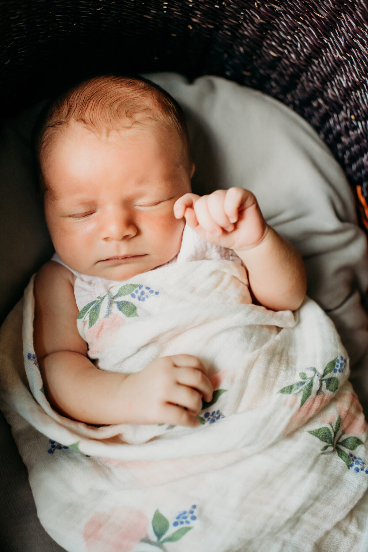Newborn Photographer, Baby girl in a swaddle blanket with her arms out, asleep in a basket.