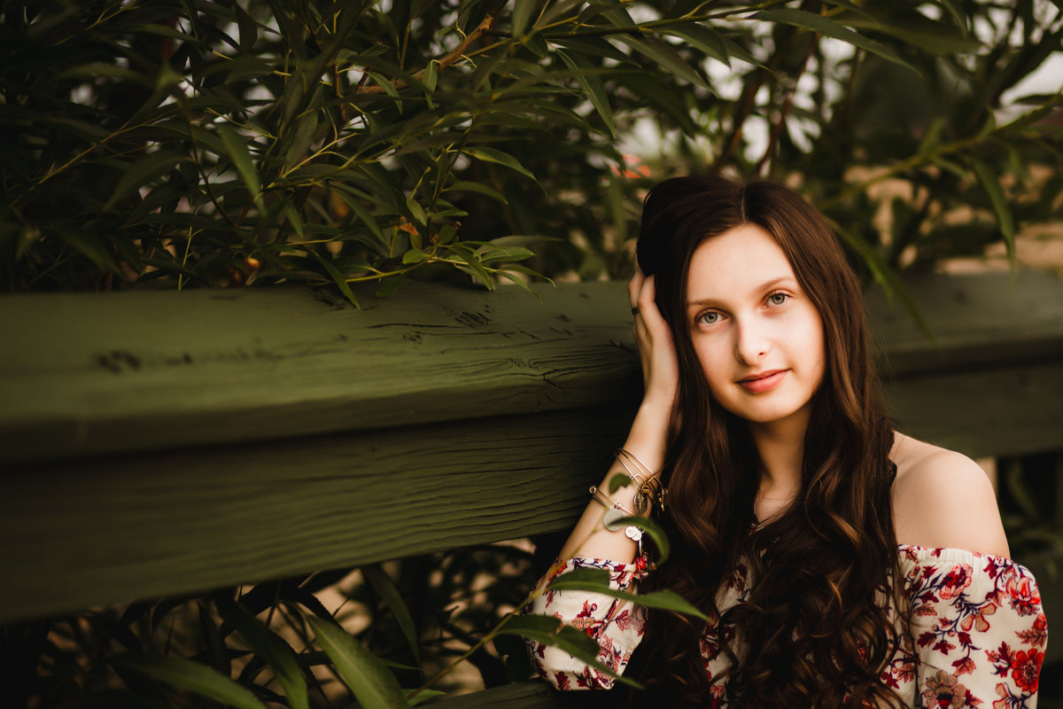teenage girl leans against green wooden bridge for senior photos in thornton colorado