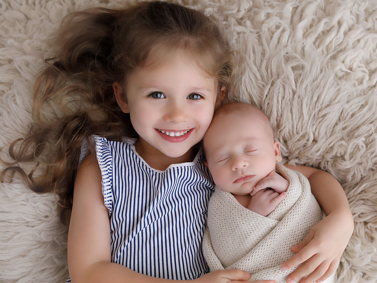 Beautiful-big-sister-holding-her-baby-brother-in-her-arms-for-his-newborn-session-and-he-is-only-9-days-old
