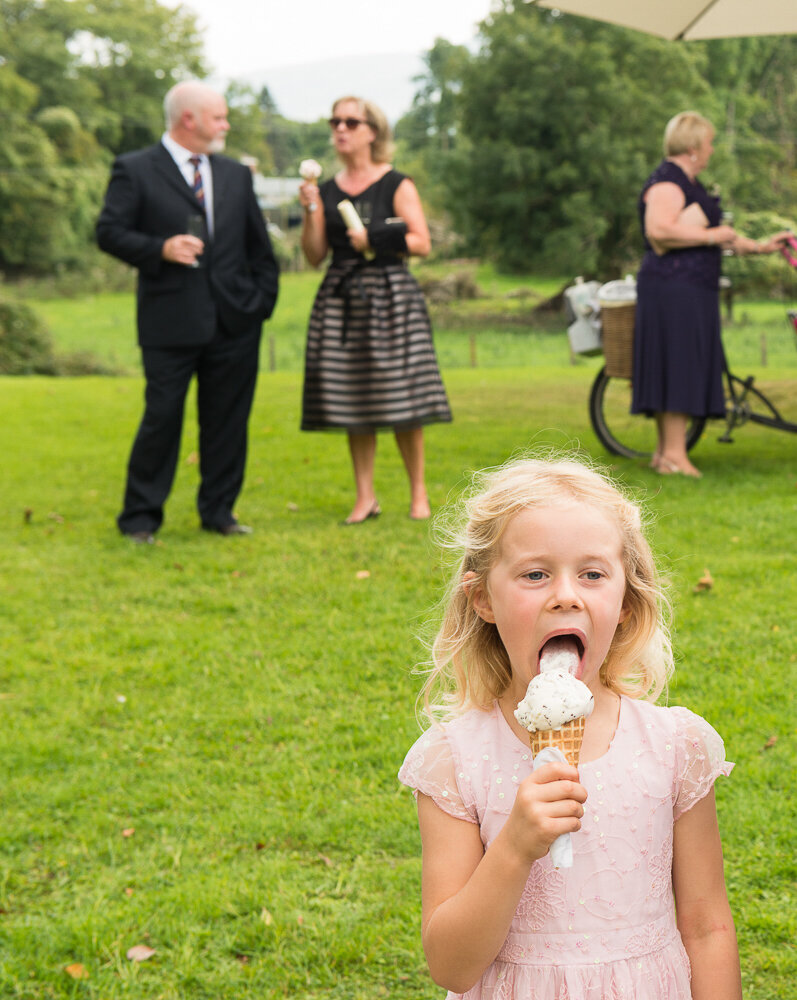 little girl in pink dress having an ice-cream in the garden with wedding guests