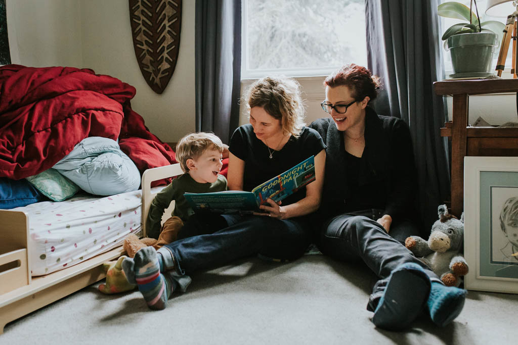 Lesbian moms read to child in bedroom during in home family photography session