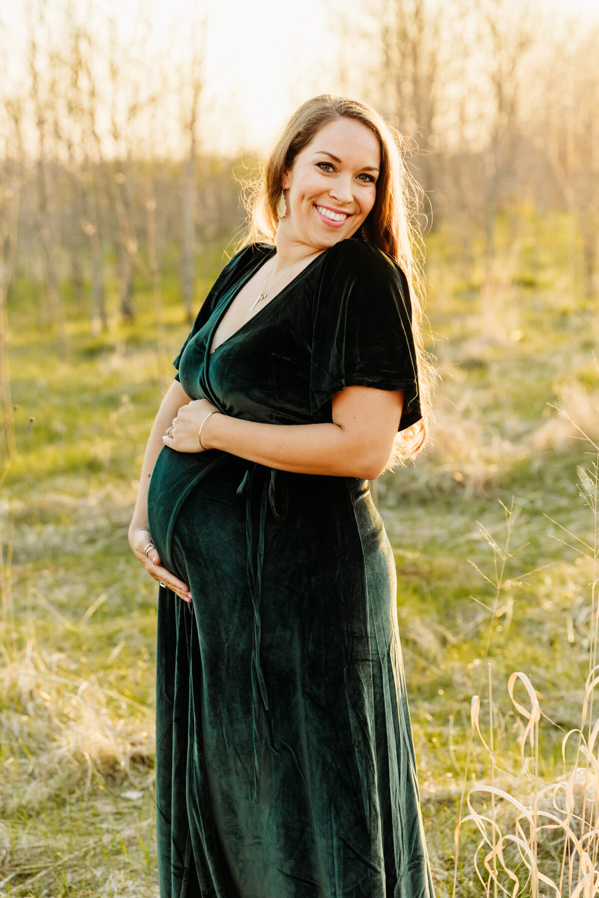 brown haired woman holding her baby bump in a field near Green Bay
