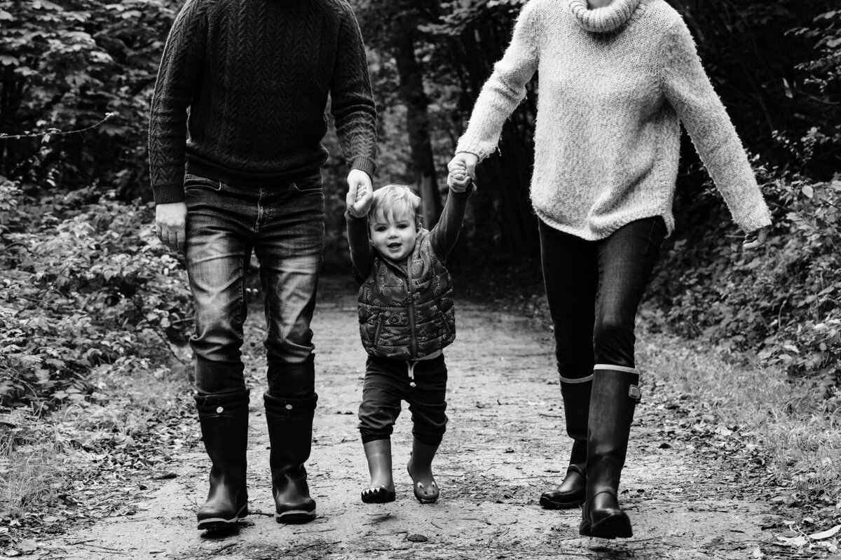 black and white image of little boy walking in barnsdale woods with mum and dad holding hands