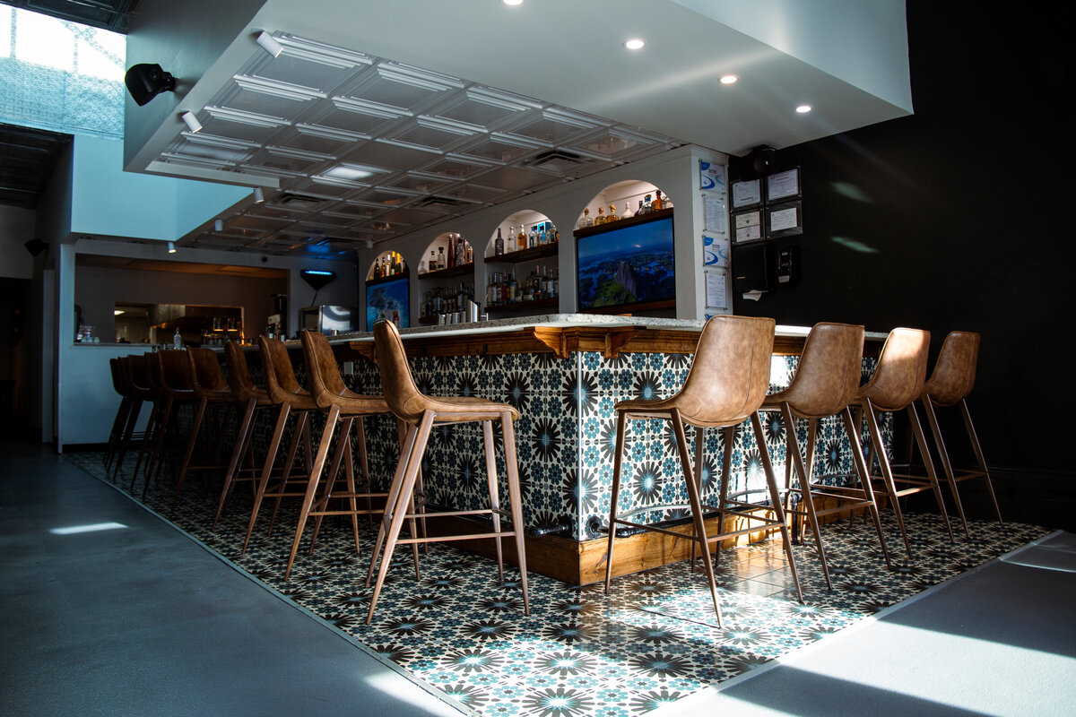 Image of a bar tiled with colorful mosaics and brown leather bar stools.
