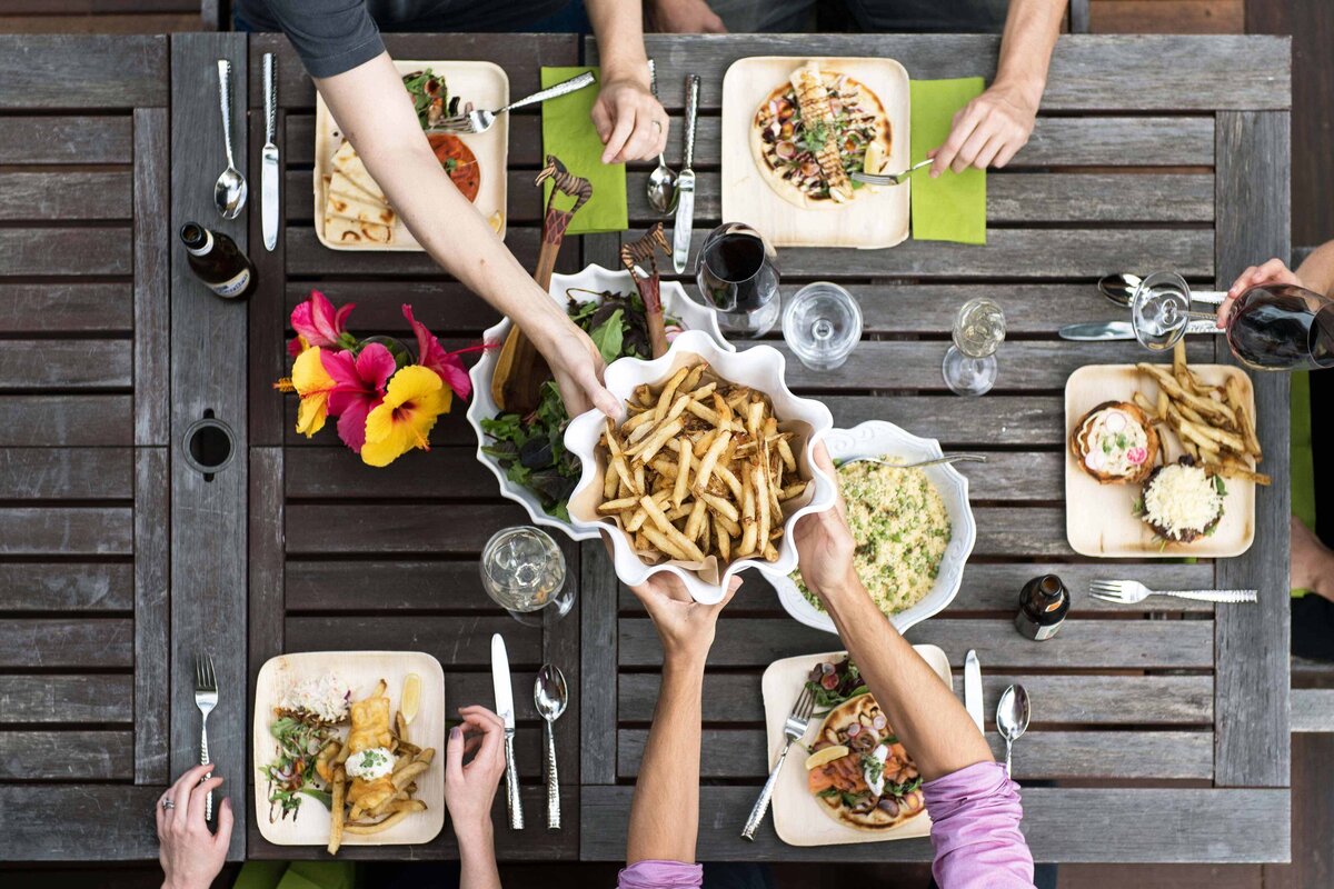 Overhead shot of hands passing french fries as other places are shown with gourmet food and wine. Marketing image for food service