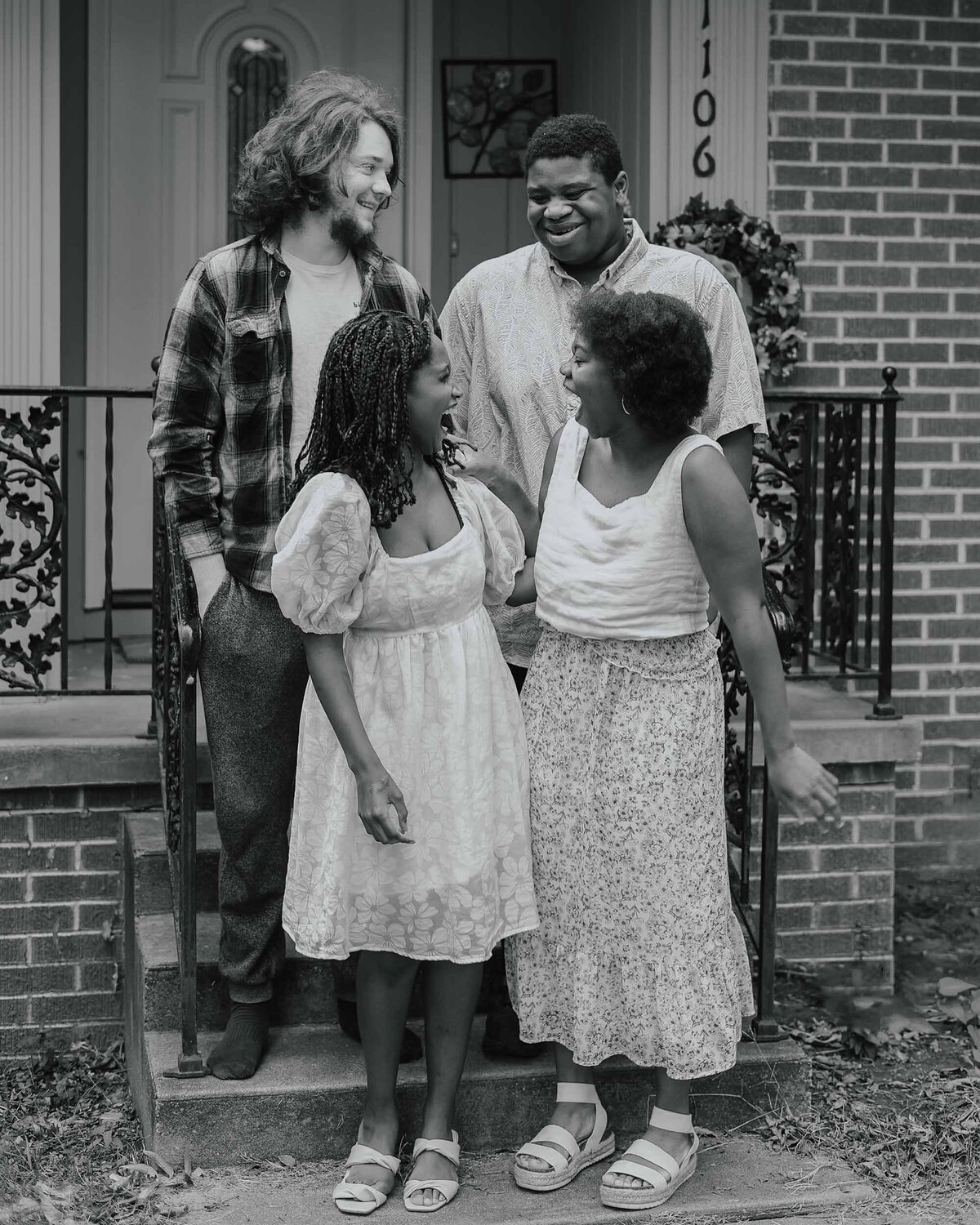 Maddie Rae Photography black and white of 4 older kids standing on the front steps, look and smiling at each other