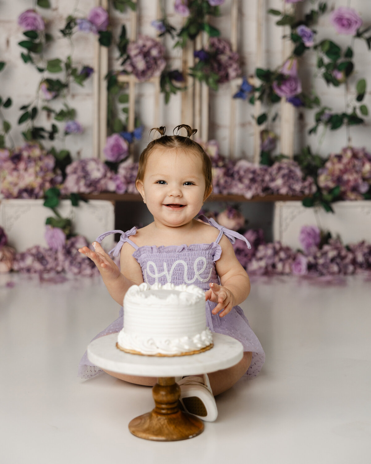 This little one is ready to dive into her cake smash session, surrounded by a dreamy purple floral backdrop. Captured by Yucaipa cake smash photographer Kaitlyn Dawn Photography.