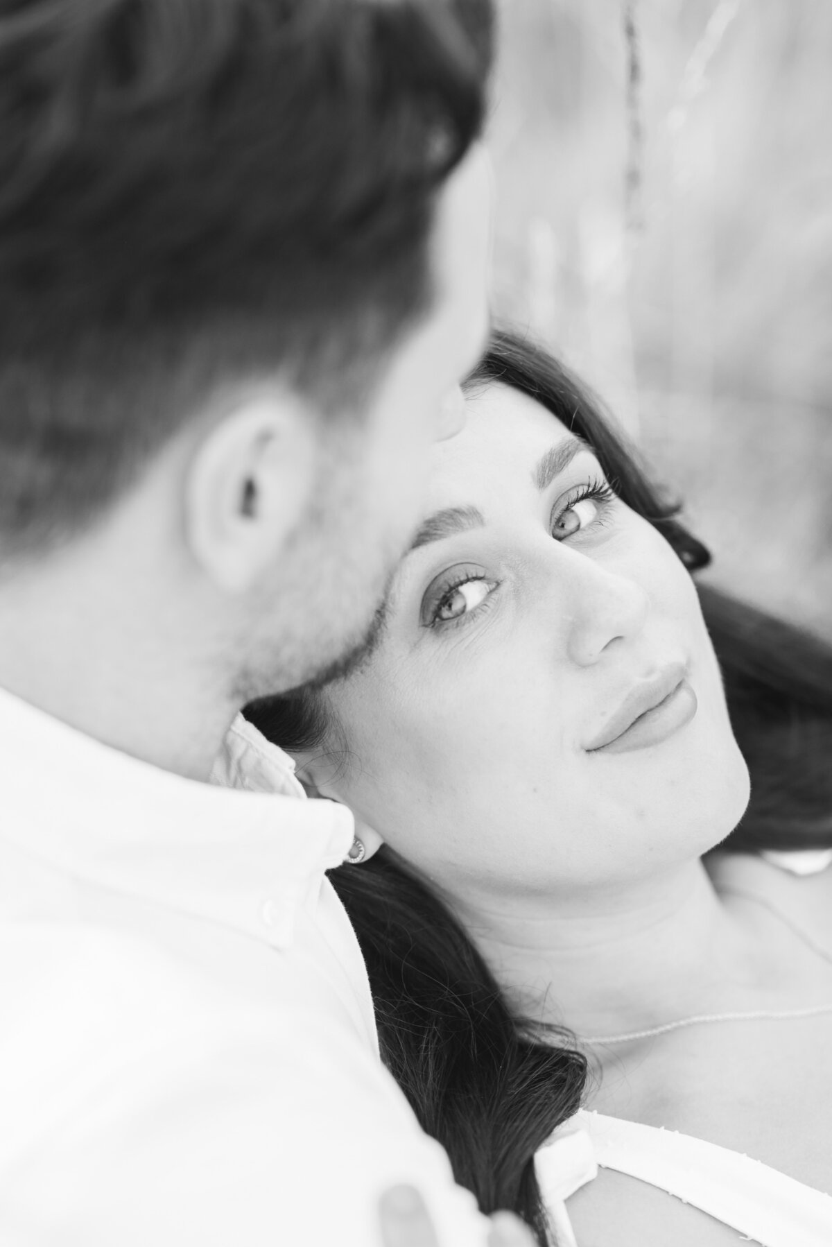 Black and white image of a couple, the girl is leant against the guy and is looking in to the camera while the guy looks loving down at her