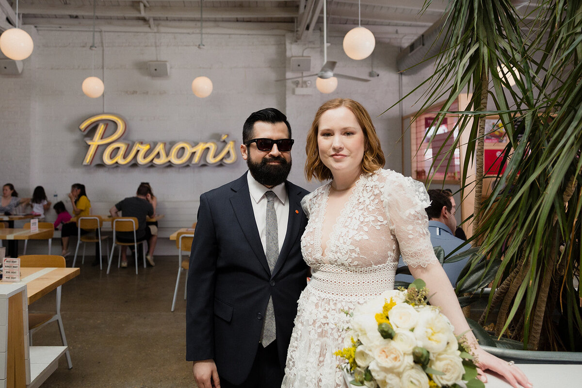 Elopement couple stands inside Parson's Chicken in Lincoln Park Chicago. Groom is wearing sunglasses, the Parson's yellow neon sign is in the background.