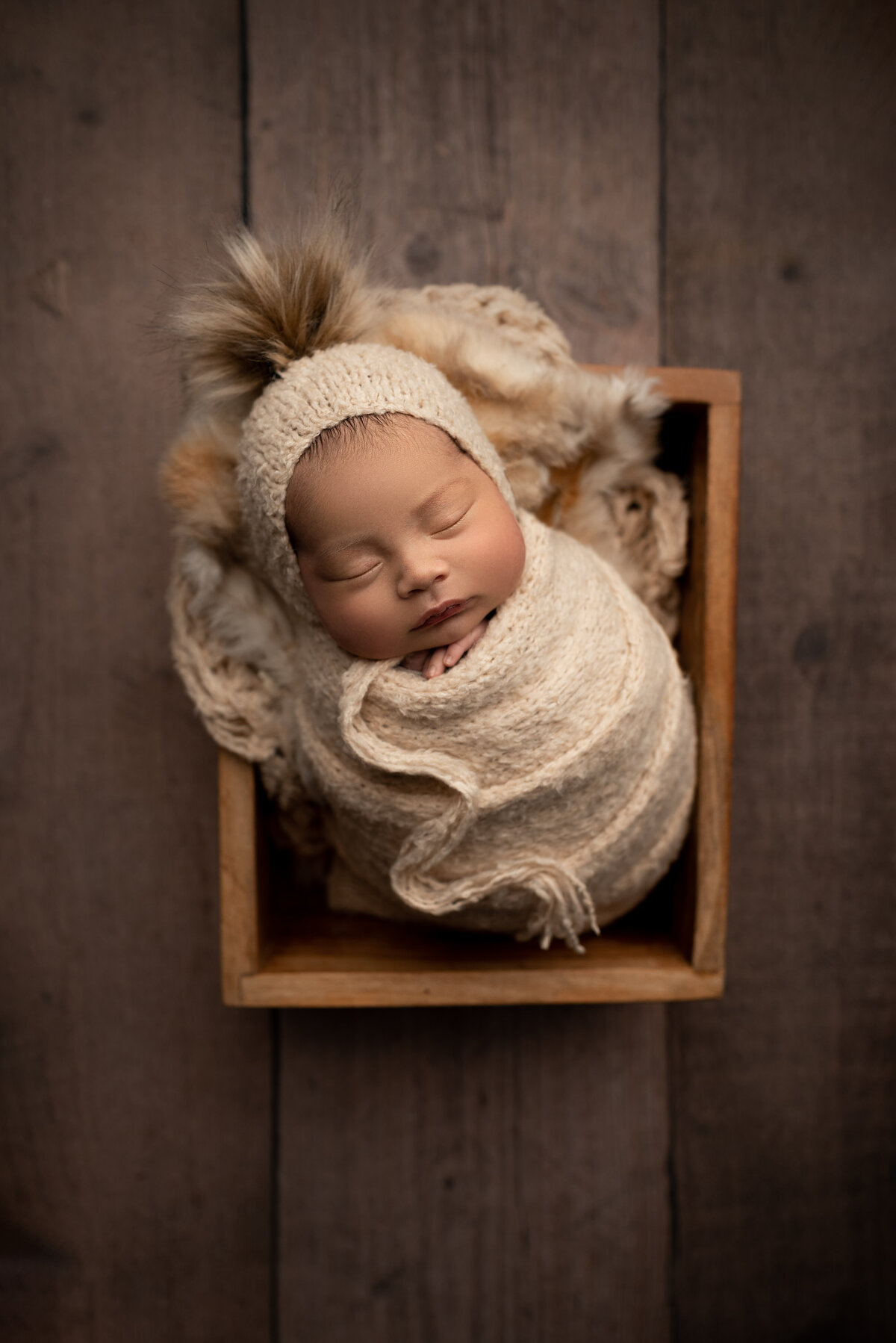 New Jersey's best newborn photographer Katie Marshall captures an aerial fine art newborn photo. Baby is swaddled in an oat-coloured knit swaddle and matching bonnet. Baby's fingers are peeking out.