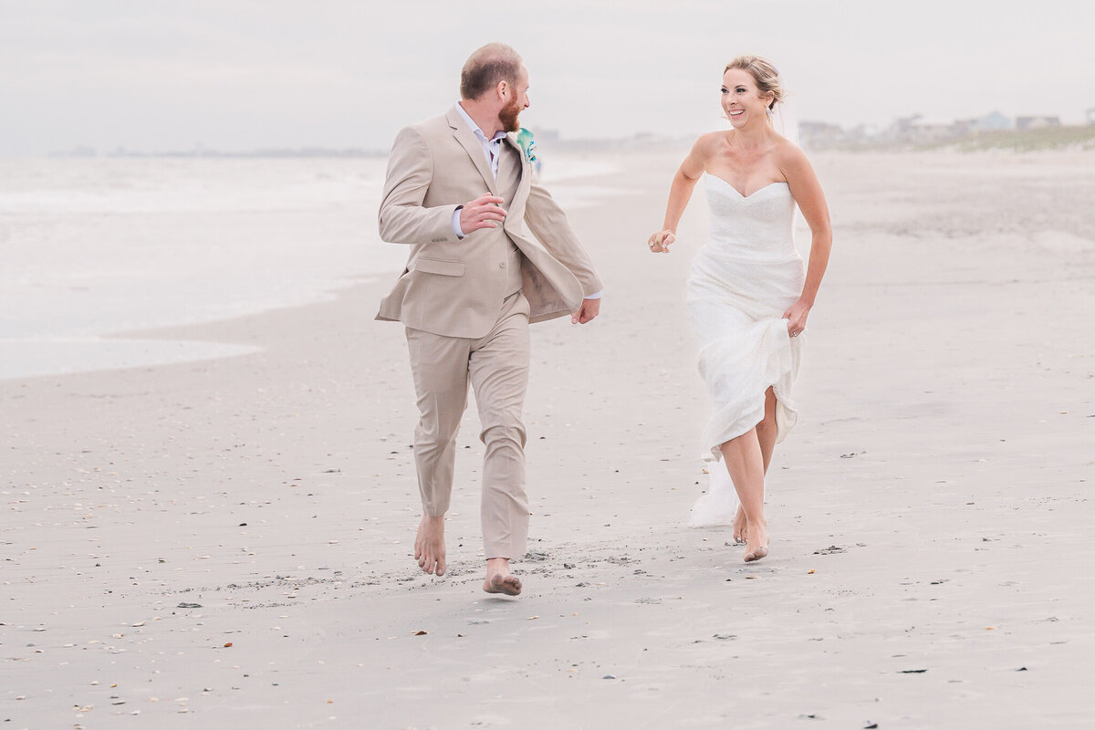 A newly married couple running on the beaches of the Outer Banks enjoying their Wilmington wedding photography by JoLynn Photography