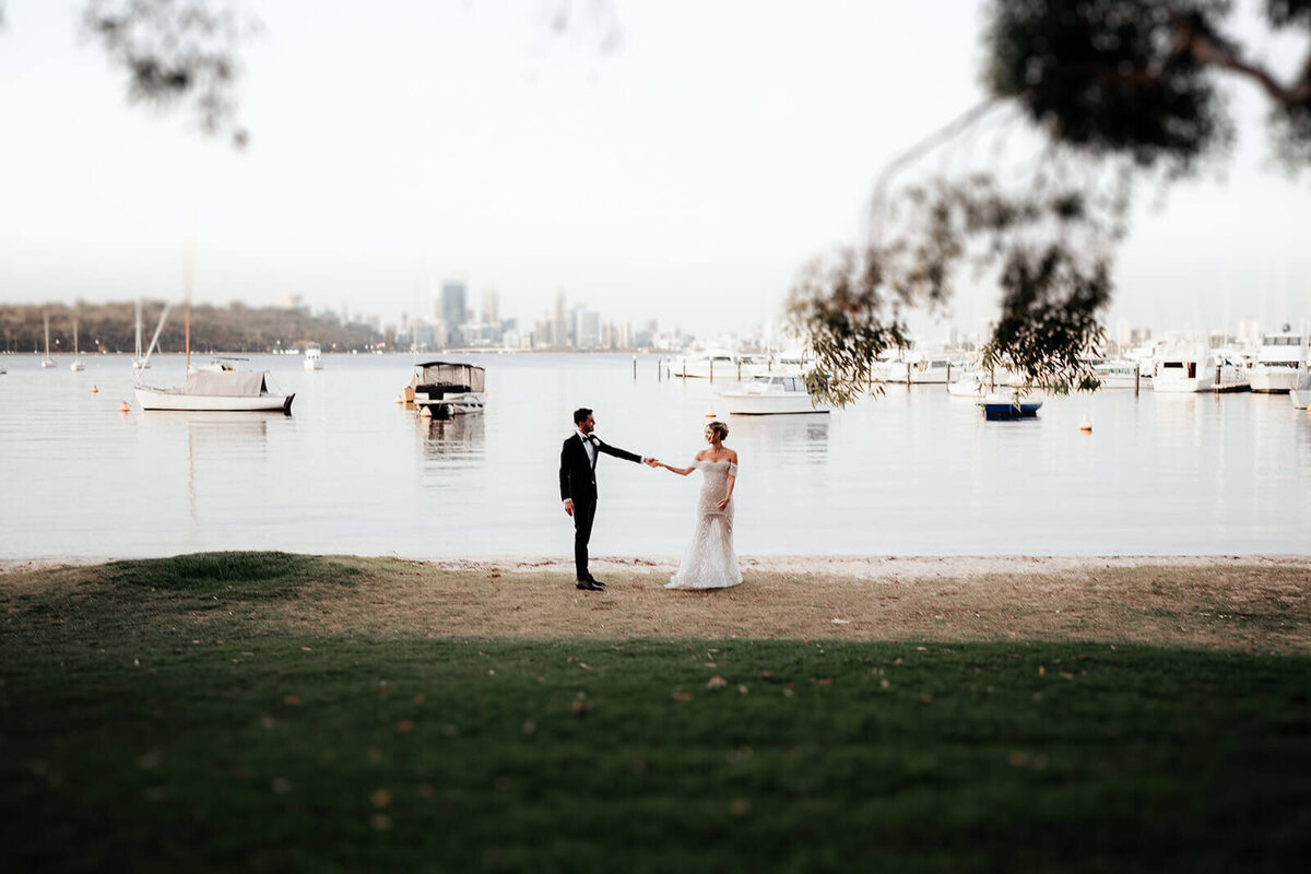 Bride and groom standing in front of the swan river with Perth city in the background