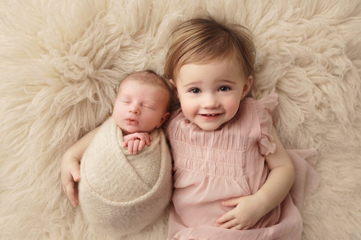 toddler girl in pink dress snuggling newborn baby in cream